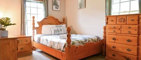 Quarto com cama de madeira, mesa de cabeceira, penteadeira e janela com cortinas.