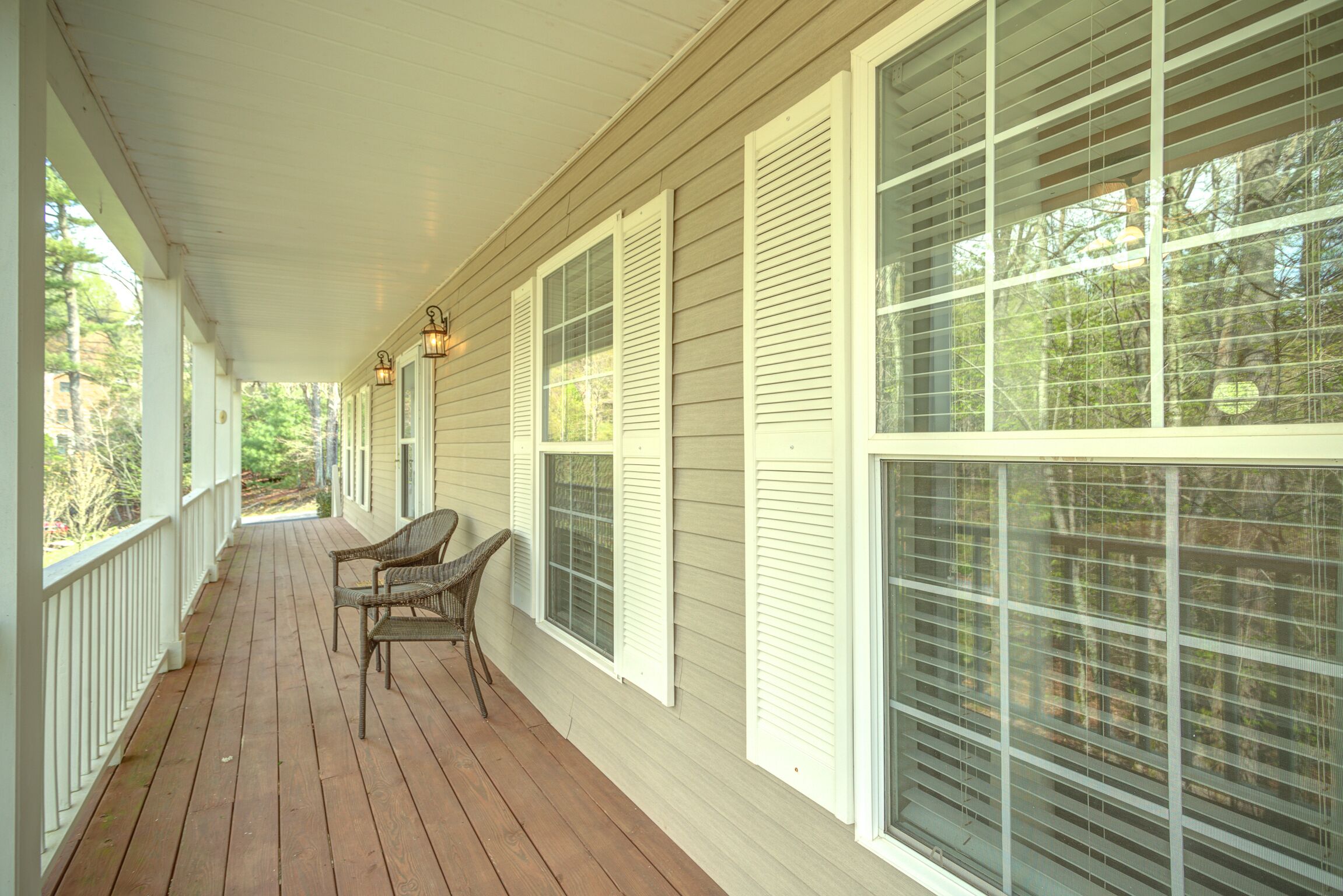 A covered porch with white railings, large windows with shutters, and wicker chairs.