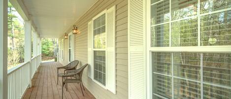 A covered porch with white railings, large windows with shutters, and wicker chairs.