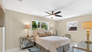 A bedroom with a bed, nightstands, a ceiling fan, a window with a view, and a lamp. - Mermaid Shack with pool 5 min to beach,venues,restaurants (Jupiter)