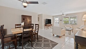 A spacious living room with a dining area, a TV, and a ceiling fan. - Mermaid Shack with pool 5 min to beach,venues,restaurants (Jupiter)