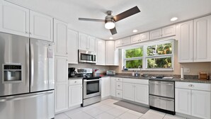 A modern kitchen with white cabinets, stainless steel appliances, a built-in microwave, and a window with a view of greenery. - Mermaid Shack with pool 5 min to beach,venues,restaurants (Jupiter)