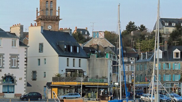 Ein Hafen mit vertäuten Booten, einem Glockenturm und Gebäuden mit Beschilderung.