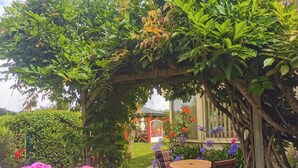 Ein Garten mit einer Holzpergola, einem Tisch mit Stühlen und verschiedenen Blumen.
