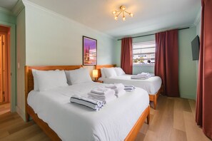 A hotel room with two beds, a nightstand with a lamp, a painting on the wall, and a window with curtains.
