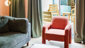 Een woonkamer met een bank, een rode fauteuil, een salontafel, een vloerlamp en een kroonluchter.