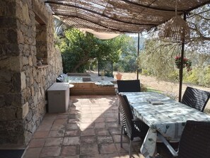 A covered patio area with stone walls, a wooden bench, a table with chairs, and potted plants. - A Picturesque Vacation Home for Nature Lovers (Belgentier)