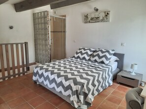 A bedroom with a bed, a nightstand, a lamp, a wooden bench, and a shower area.