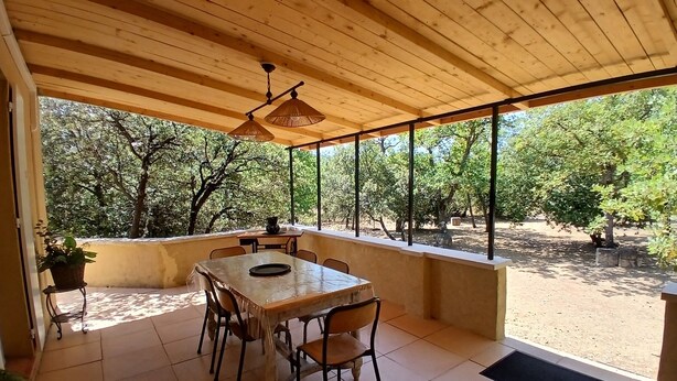 A covered patio area with a table and chairs, large windows, and a view of trees.