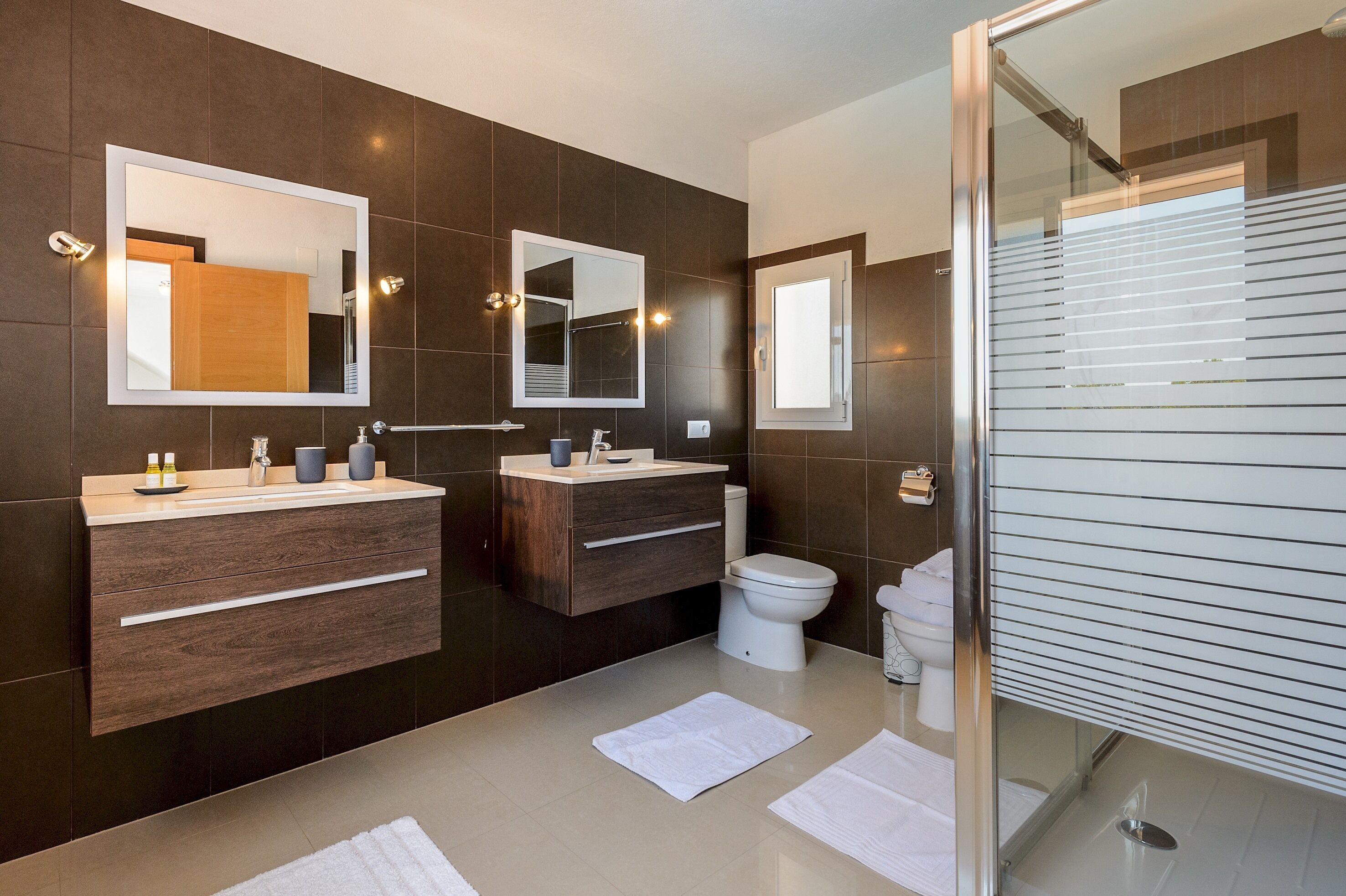Een moderne badkamer met twee wasbakken, een toilet en een douche.
