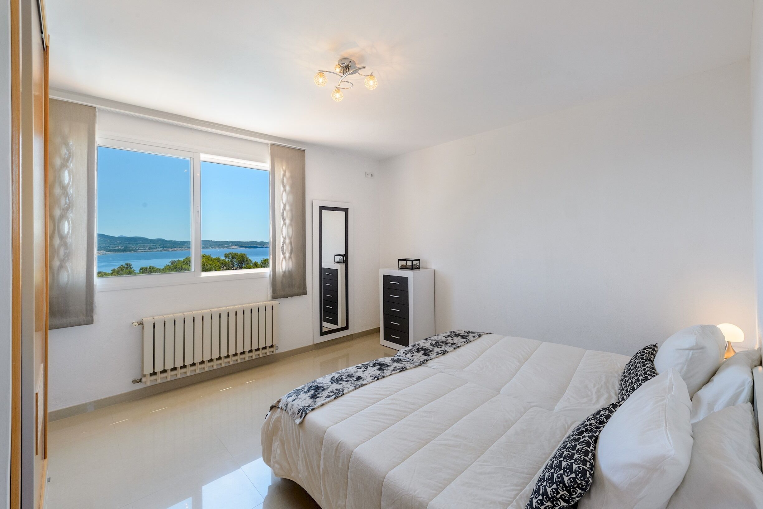 Une chambre avec un grand lit, un radiateur, une armoire et une vue sur la mer.
