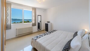 A bedroom with a large bed, a radiator, a wardrobe, and a view of the sea. - Villa Las Tres Yucas (Sant Antoni de Portmany)