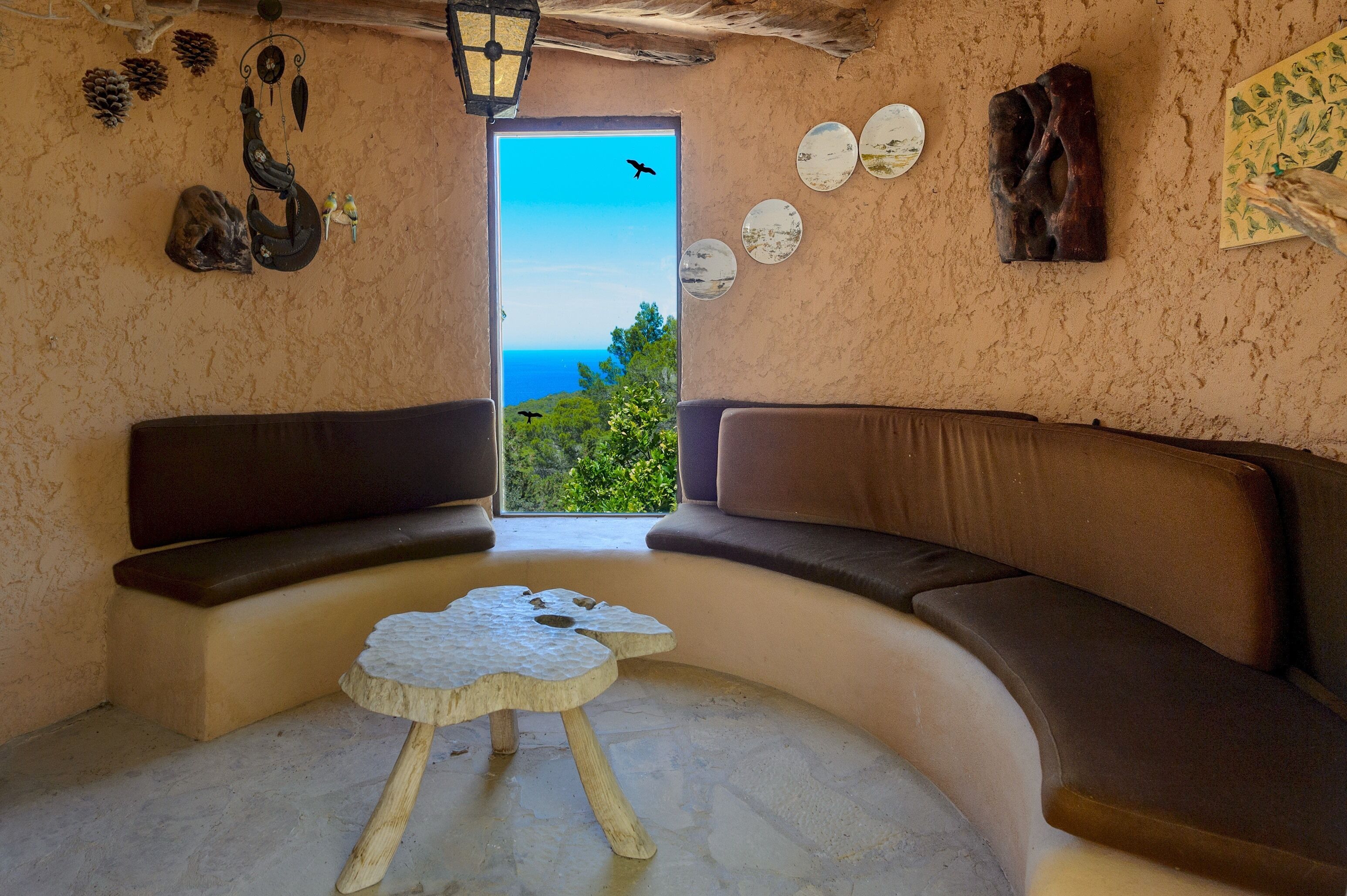 Une pièce chaleureuse avec un canapé incurvé, une petite table ronde et une vue sur la mer par une grande fenêtre.