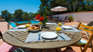 A round wooden table set for breakfast with croissants, orange juice, and a bowl of fruit. - Villa Las Tres Yucas (Sant Antoni de Portmany)
