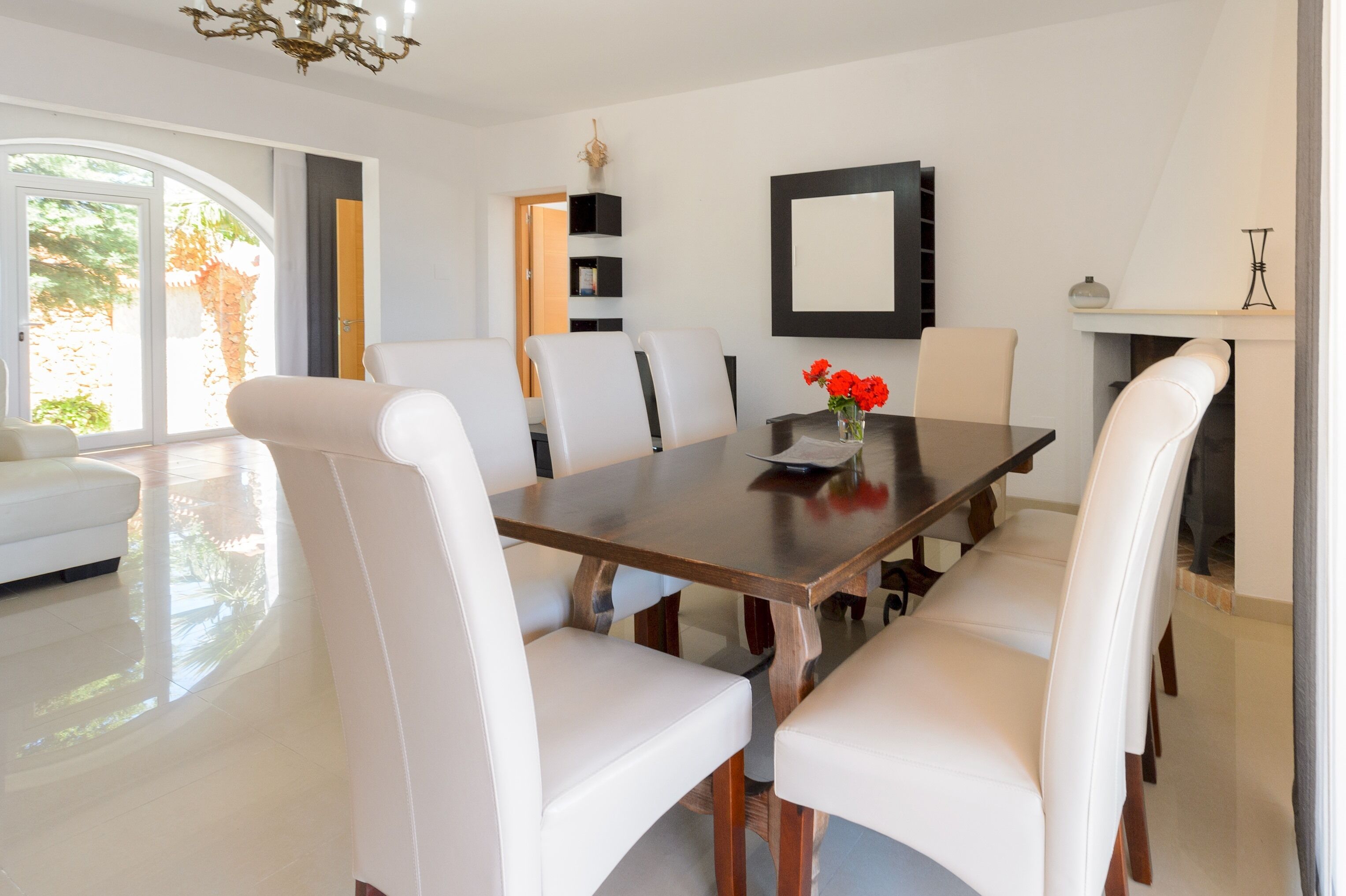 Une salle à manger moderne avec une grande table en bois, des chaises à revêtement blanc et un vase rempli de fleurs rouges.