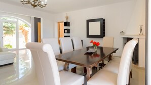 A modern dining room with a large wooden table, white upholstered chairs, and a vase of red flowers. - Villa Las Tres Yucas (Sant Antoni de Portmany)