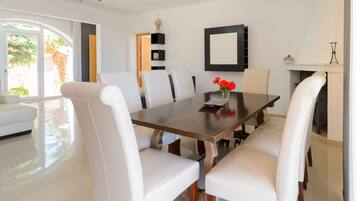 Une salle à manger moderne avec une grande table en bois, des chaises à revêtement blanc et un vase rempli de fleurs rouges.