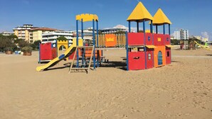 Ein Strandspielplatz mit Klettergerüsten und Rutschen, vor einer Kulisse aus Gebäuden und blauem Himmel.