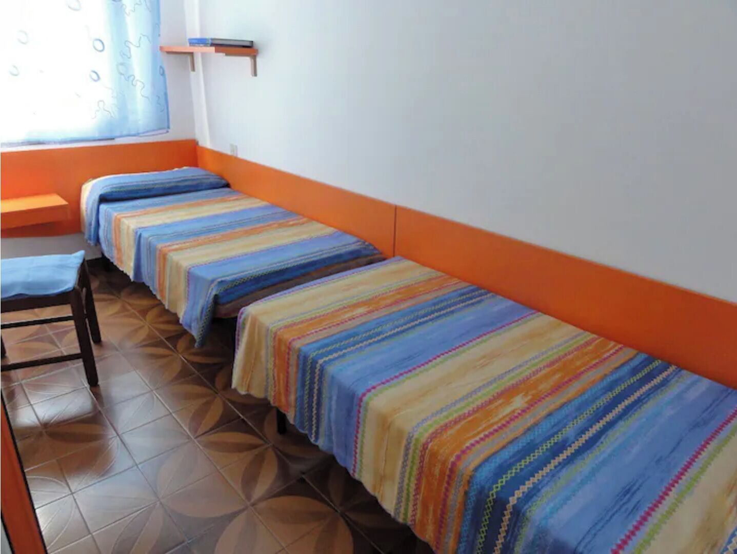 Una habitación con cuatro camas alineadas contra la pared, cada una con una colcha a rayas de colores.