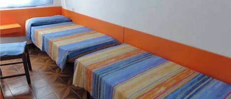 Una habitación con cuatro camas alineadas contra la pared, cada una con una colcha a rayas de colores.