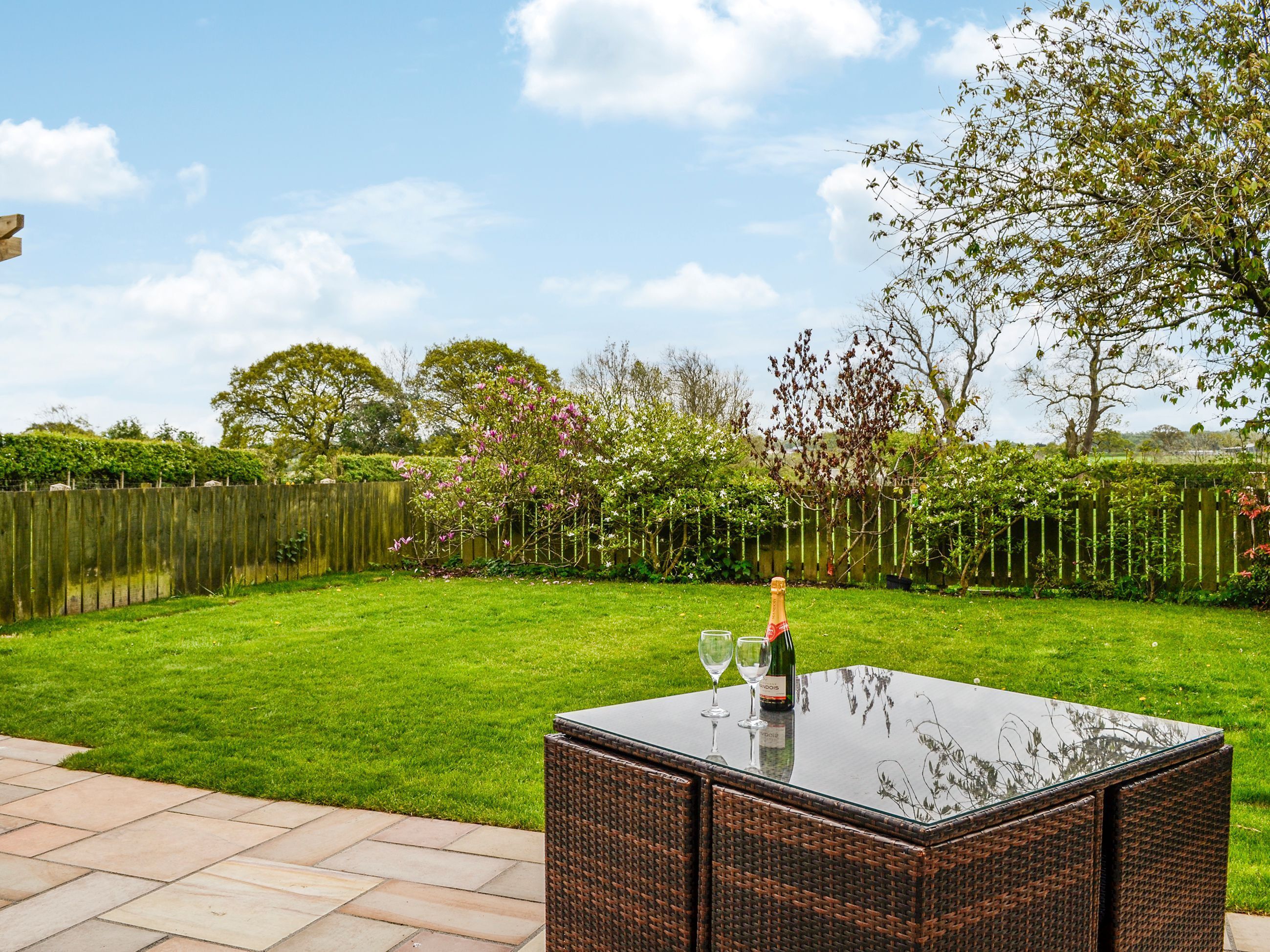 A patio with a glass-top table, two wine glasses, and a bottle of champagne.