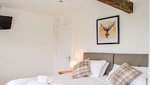 Een net opgemaakt bed met witte linnens en opgerolde handdoeken, een hoofdeinde en een kunstwerk met een hertenhoofd aan de muur.