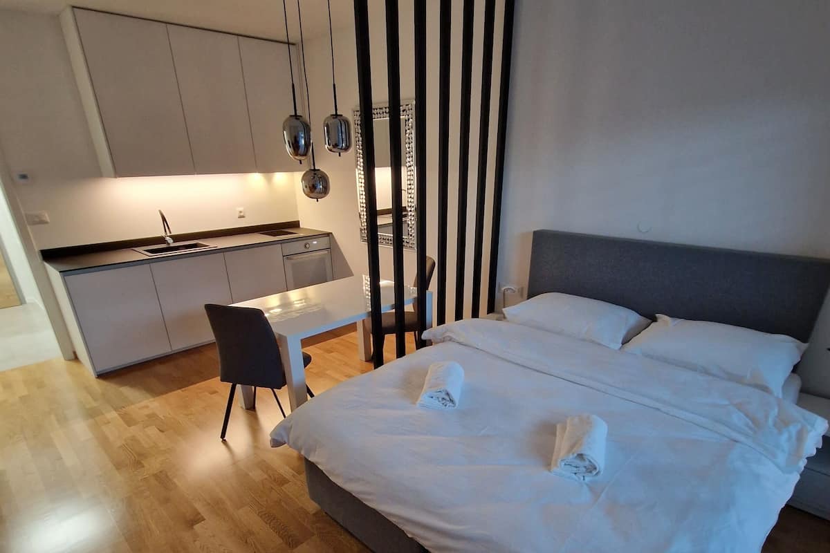 A modern hotel room with a large bed, a desk, and a kitchenette.
