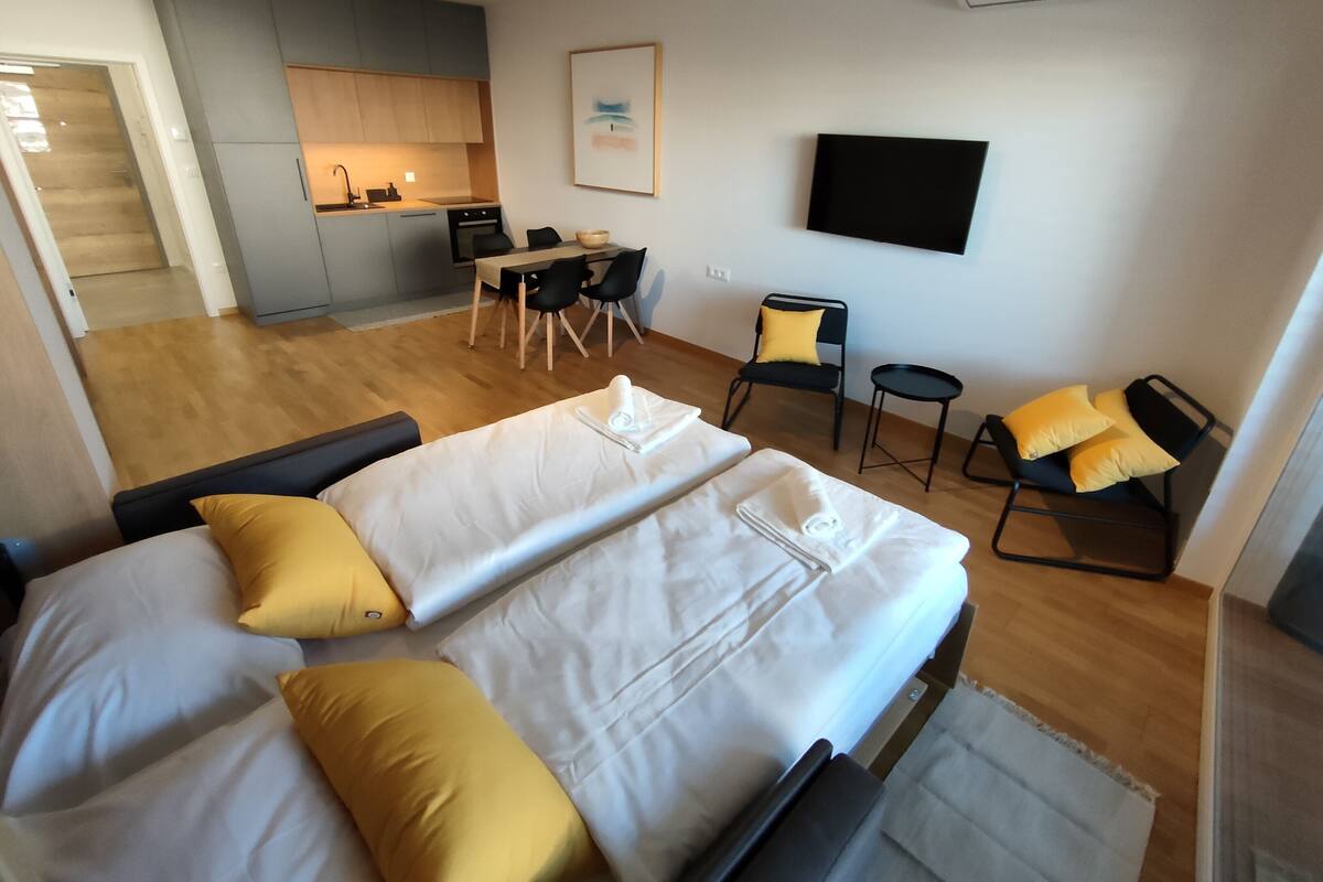 A modern hotel room with a large bed, a desk, a chair, and a kitchenette.