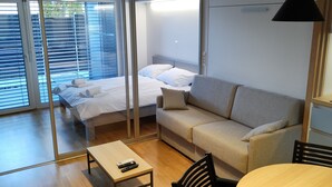 A modern hotel room with a bed, a sofa, a dining table, and a large window. - REZIDENCA PIPANOVA (Ljubljana)