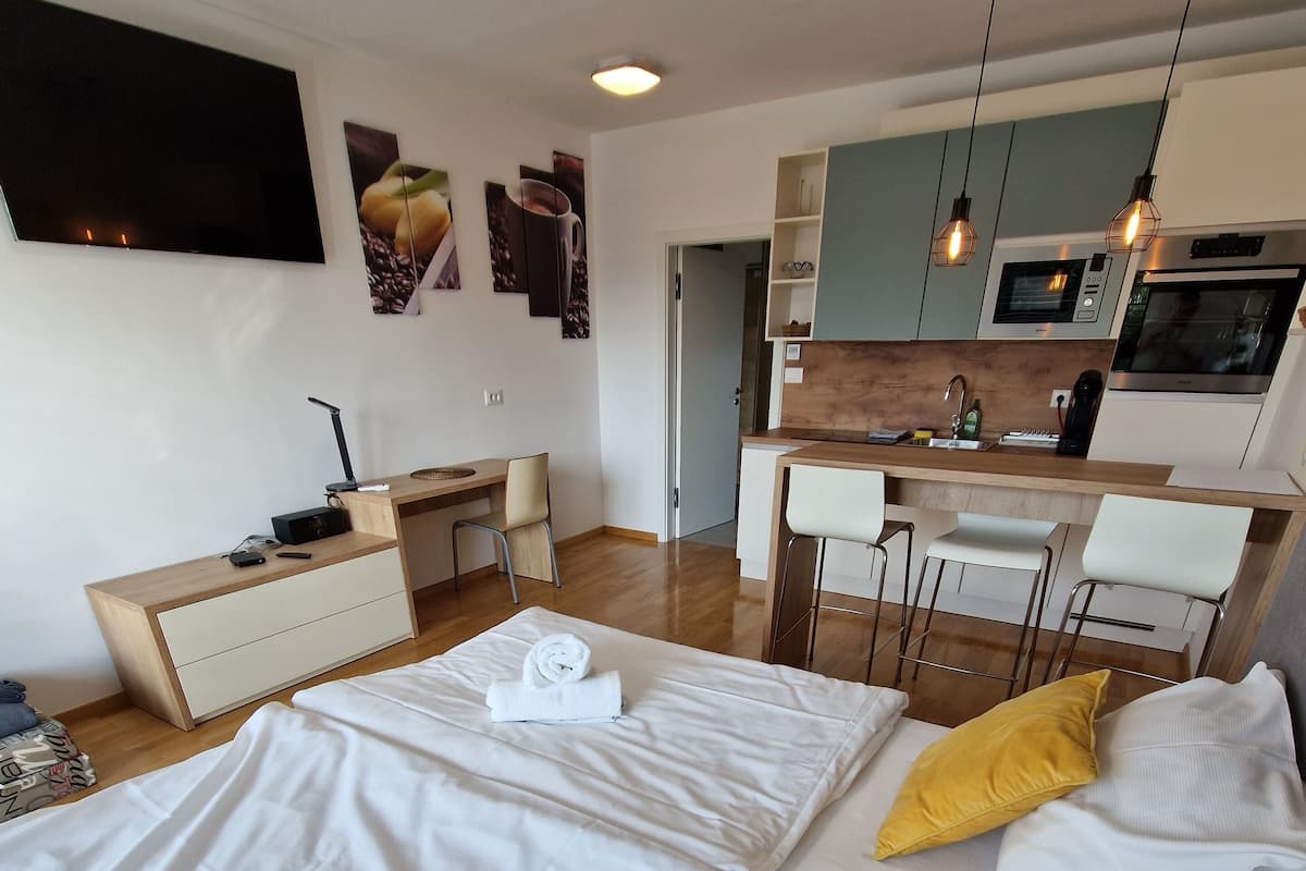 A modern hotel room with a bed, a desk, a kitchenette, and a dining area.