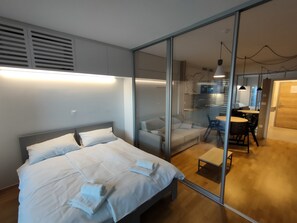 A modern hotel room with a bed, a glass partition, a dining area, and a kitchen visible through the glass. - REZIDENCA PIPANOVA (Ljubljana)