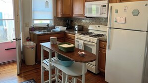 A kitchen with wooden cabinets, a microwave, a stove, and a refrigerator. There is a window with blinds, a sink, and a countertop with a toaster and a coffee maker. - Beach Haven Long Beach Island (Beach Haven)