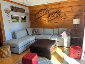 Relax in this inviting space with a large L-shaped sofa and matching ottoman, complemented by a wooden coffee table and side table with a lamp.
