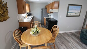Een compacte keuken met houten kastjes, een koelkast en een eethoek met een houten tafel en stoelen.