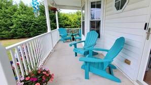 Varanda com cadeiras Adirondack turquesa, uma mesa pequena e corrimão branco.