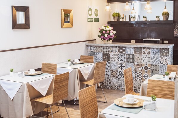 Un restaurante con varias mesas, sillas, una barra con salpicadero de azulejos y adornos en la pared.