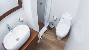 A bathroom with a white sink, wooden vanity, white toilet, and a shower area.