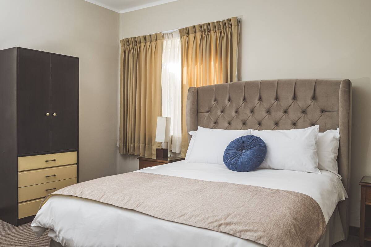 A neatly arranged hotel room with a large bed, a wardrobe, and a nightstand.