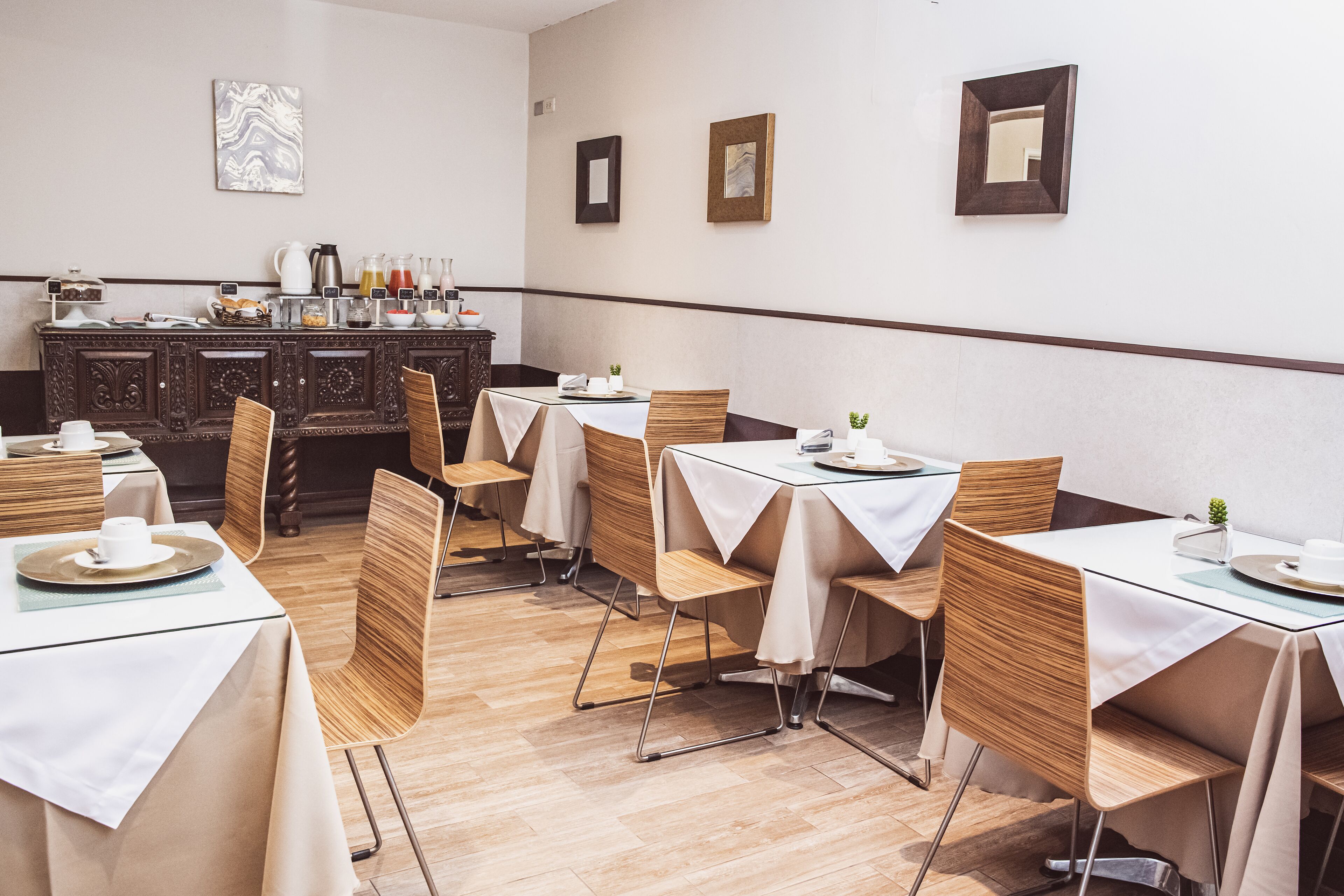 Comedor con mesas dispuestas para cuatro, sillas de madera y un mostrador tipo buffet al fondo.