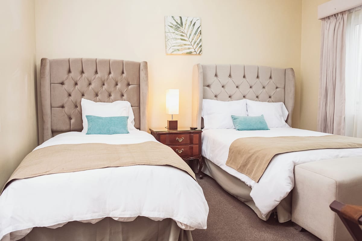 A hotel room with two beds, a nightstand, a lamp, and a leaf artwork on the wall.