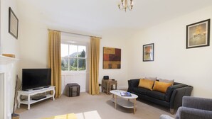 A living room with a television, sofa, armchairs, a coffee table, and a window with curtains.