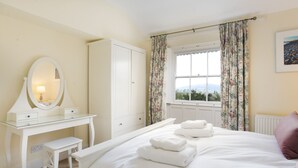 A bedroom with a bed, a bedside table, a mirror, a wardrobe, and a window with curtains.