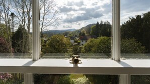 A view through a window with a brass handle, overlooking a landscape with houses, trees, and hills.