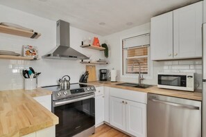 Cocina moderna con armarios blancos, extractor de acero inoxidable, microondas y lavavajillas.