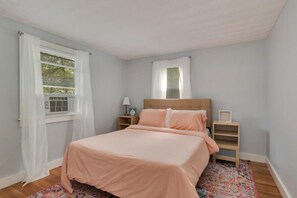A bedroom with a bed, bedside tables, a nightstand, a window with curtains, and a radiator.
