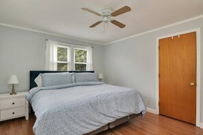 A bedroom with a bed, a nightstand, a window, a door, and a ceiling fan.