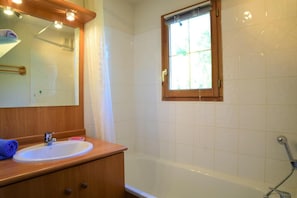 Une salle de bain avec un meuble-lavabo en bois, un évier, un miroir, une fenêtre et une baignoire.