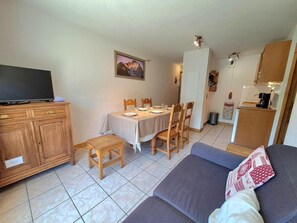 A compact living space with a dining area, a sofa, a television, and a kitchenette.