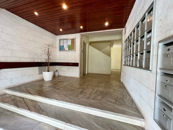 A lobby with a marble floor, a potted plant, a bulletin board, and a row of mailboxes.