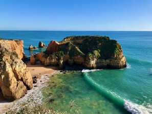 A coastal landscape with rocky cliffs, clear turquoise waters, and a sandy beach.